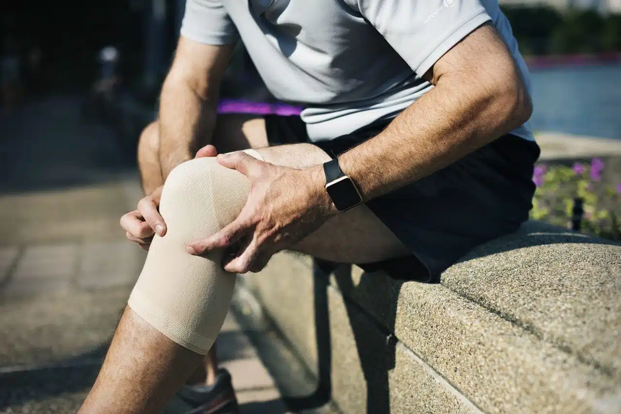 A man with a knee brace sitting on a ledge experiencing knee pain