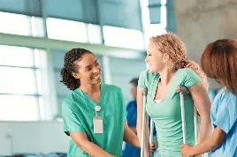 two female nurses helping a woman on crutches