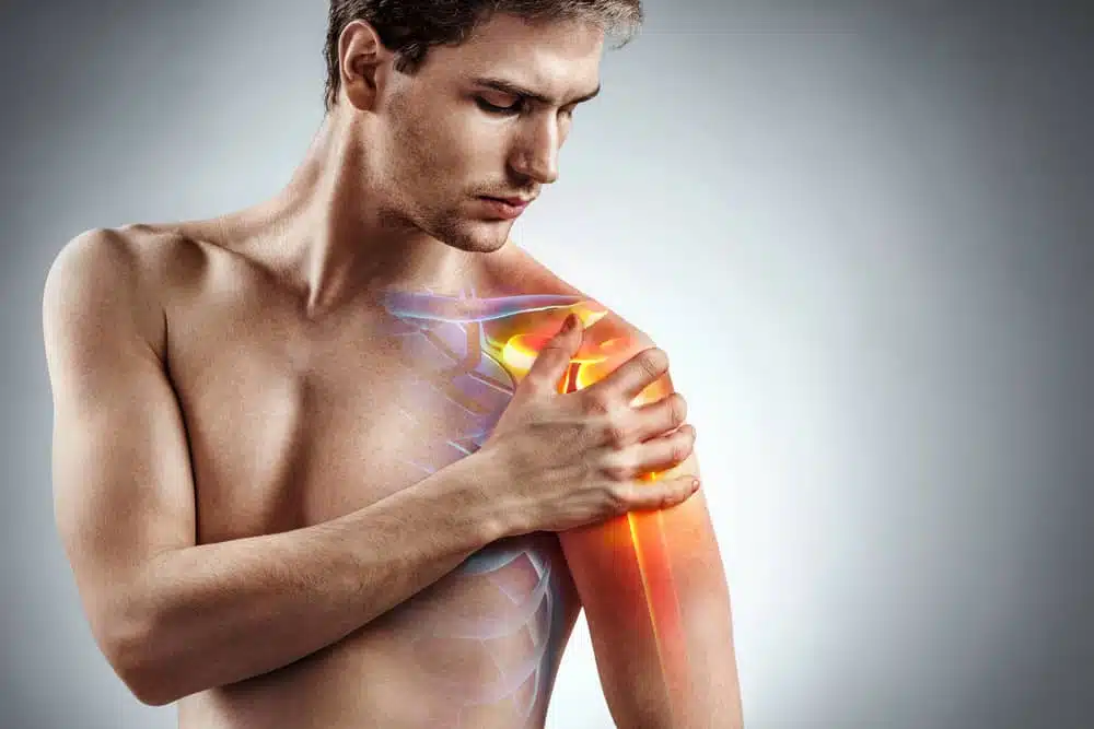 Mascular man holding his shoulder for burning sensation caused by shoulder pain.