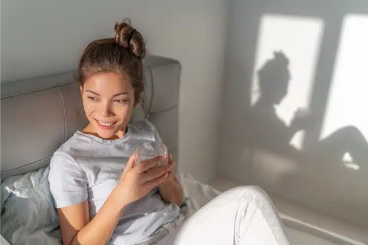 Woman drinking a glass of water feeling happy after waking up   with  pain relief in her body.