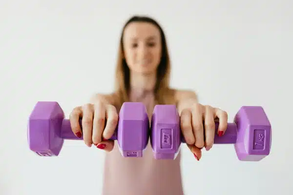 Purple dumbbells in hands of positive sportswoman